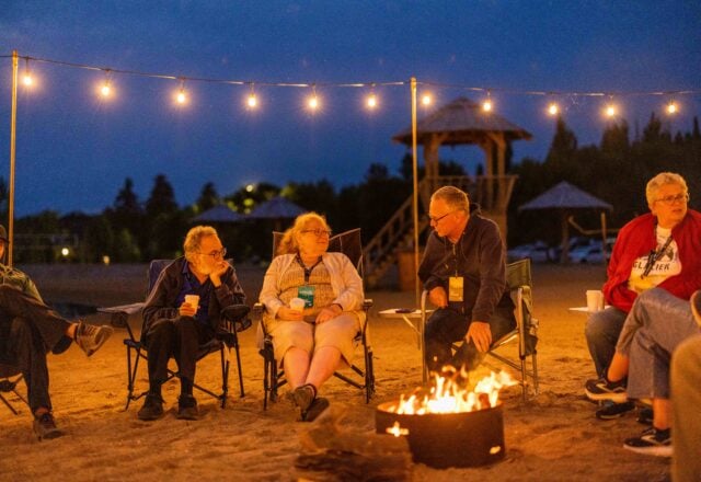 attendees sit around a campfire on the beach